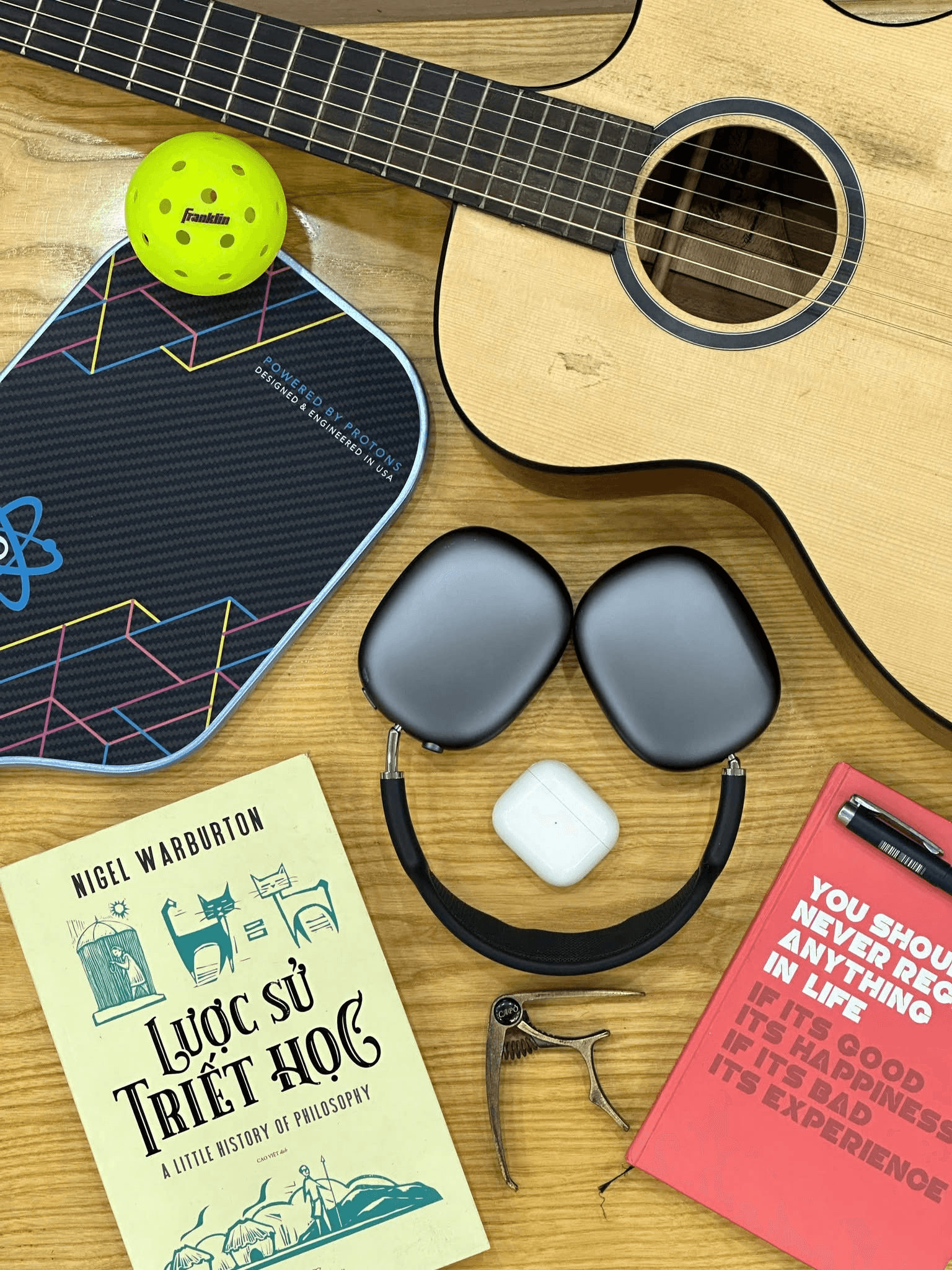 Góc bàn làm việc của Kai với đàn guitar, sách, tai nghe và vợt pickleball